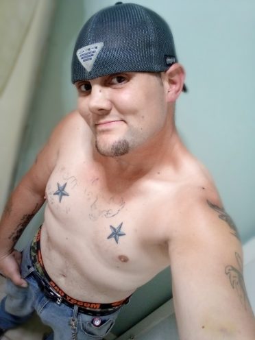 Guy with hat on backwards, shirtless with tattoos taking selfie
